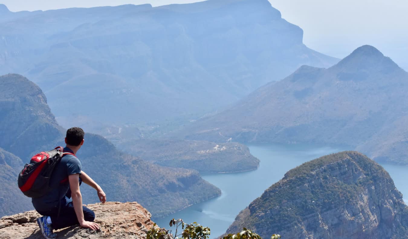 Nomadic Matt kneeling on a cliff looking out over a huge valley in South Africa