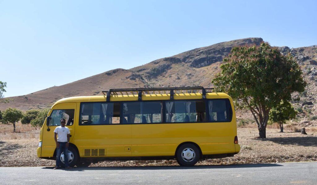 A bus driver stands by his yellow bus by the side of the road in Africa