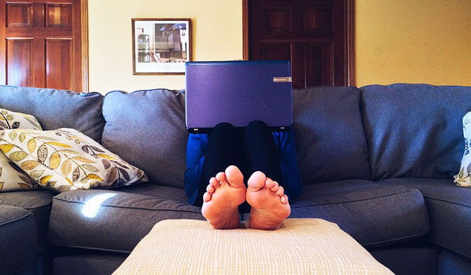 Man on a couch with feet up towards the camera face obstructed by laptop