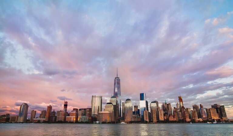 A photo of the towering Manhattan skyline at dusk with light pink clouds overhead