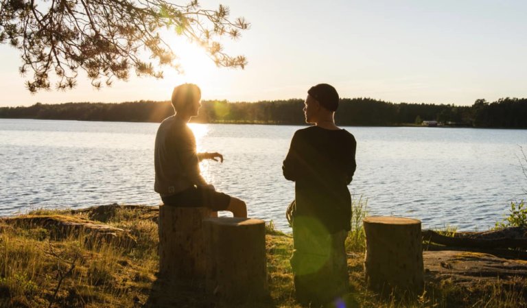 Two travelers having a conversation by a lake