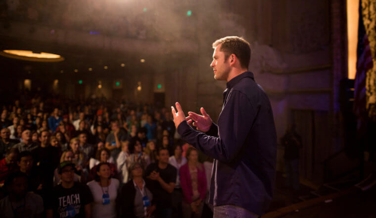 Chris Guillebeau on stage speaking to a large crowd