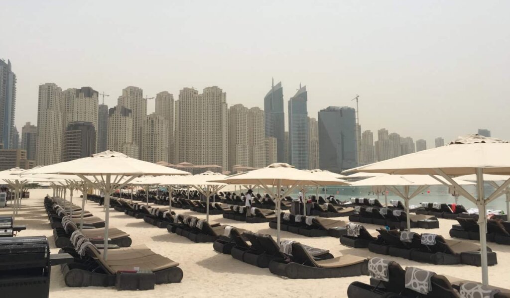 Rows of loungers and umbrellas on the sand in Dubai with a skyline of skyscrapers in the background