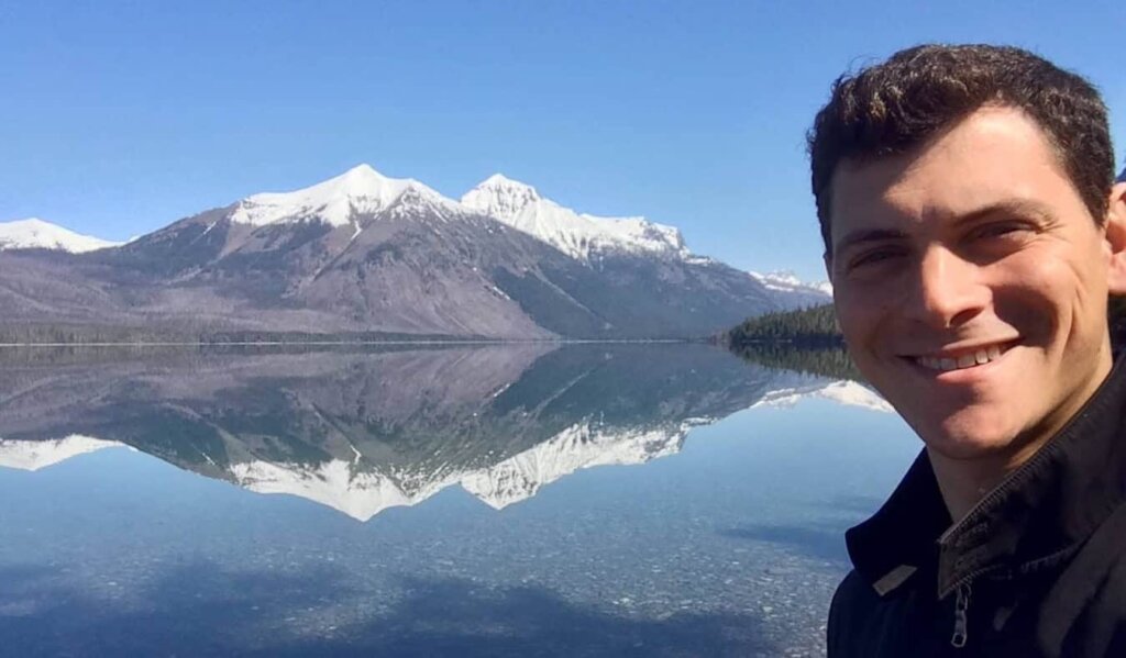 Nomadic Matt posing near snow-caped mountains in sunny USA on a road trip