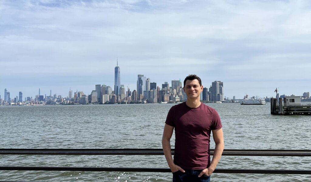 Nomadic Matt leaning on a railing with the Manhattan skyline behind him