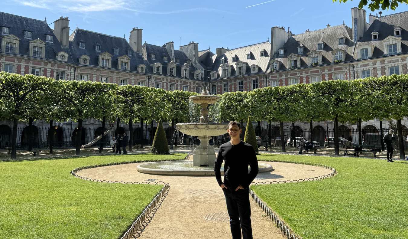 Nomadic Matt standing in the Place de Vosages, a large enclosed square surrounded by buildings, with a fountain in the middle, in Paris, France