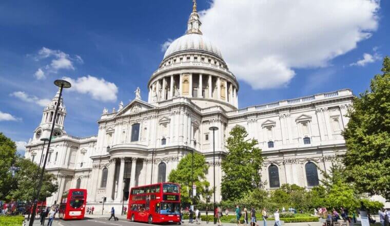 Front view of the domed St. Paul's cathedral, with double decker red buses and people walking in front of it in London, England