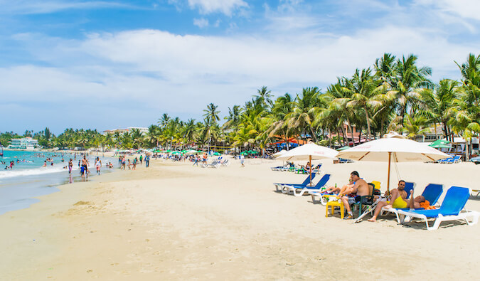 people lounging on a busy beach lined with palm trees