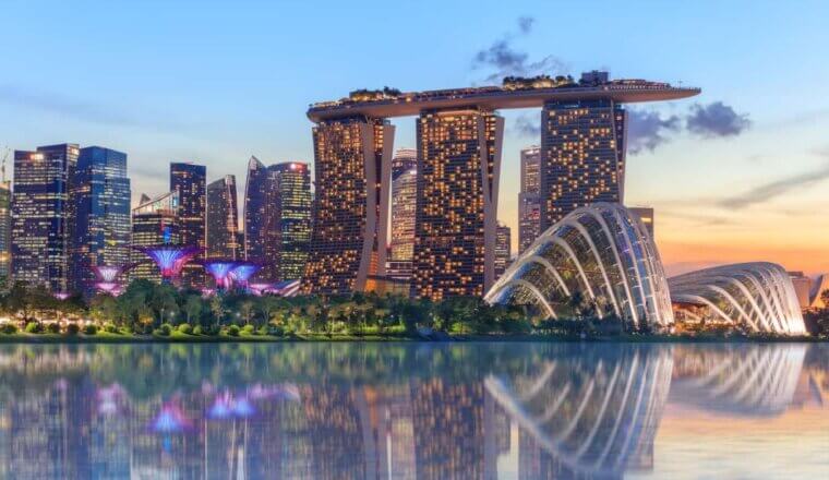 Singapore's supertree grove, cloud garden greenhouse and Marina Bay Sands hotel reflecting in water at dusk with glowing lights